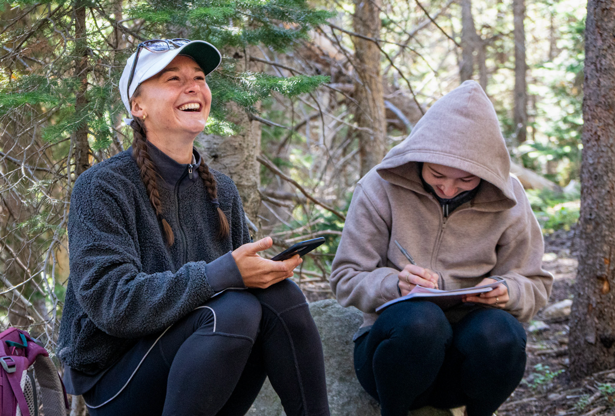 Two graduates from the Certificate in Communications for Conservation laugh while sitting in the forest